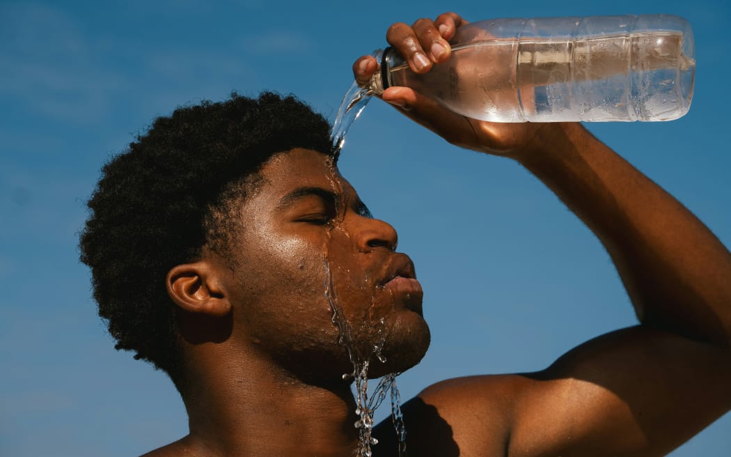 A man pours water from a bottle on his head on a hot summer day outdoors.