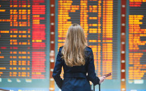 Young woman in international airport looking at the flight information board, holding passport in her hand, checking her flight