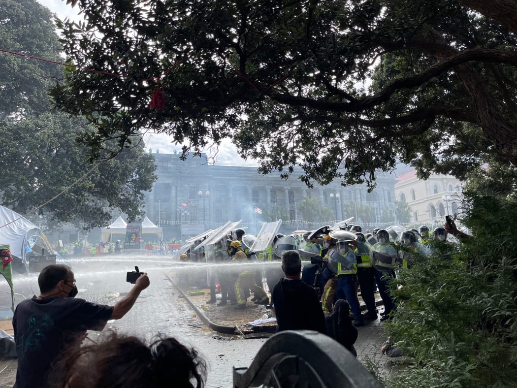 Police using hoses on the fire from behind riot shields.