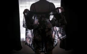 Woman stands silhouetted against window in lingeries and drapy wrap