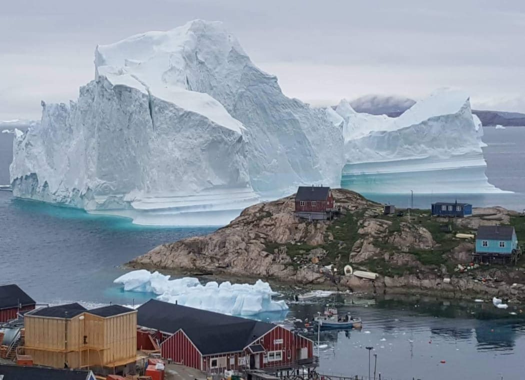 An iceberg behind houses and buildings after it grounded outside the village of Innarsuit, an island settlement in the Avannaata municipality in northwestern Greenland.