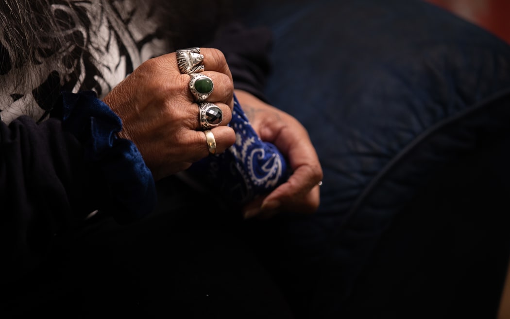 Joyce Harris, photograhed during an interview with RNZ in her living room. She sits in an armchair, holding a blue bandana tightly in her hands.