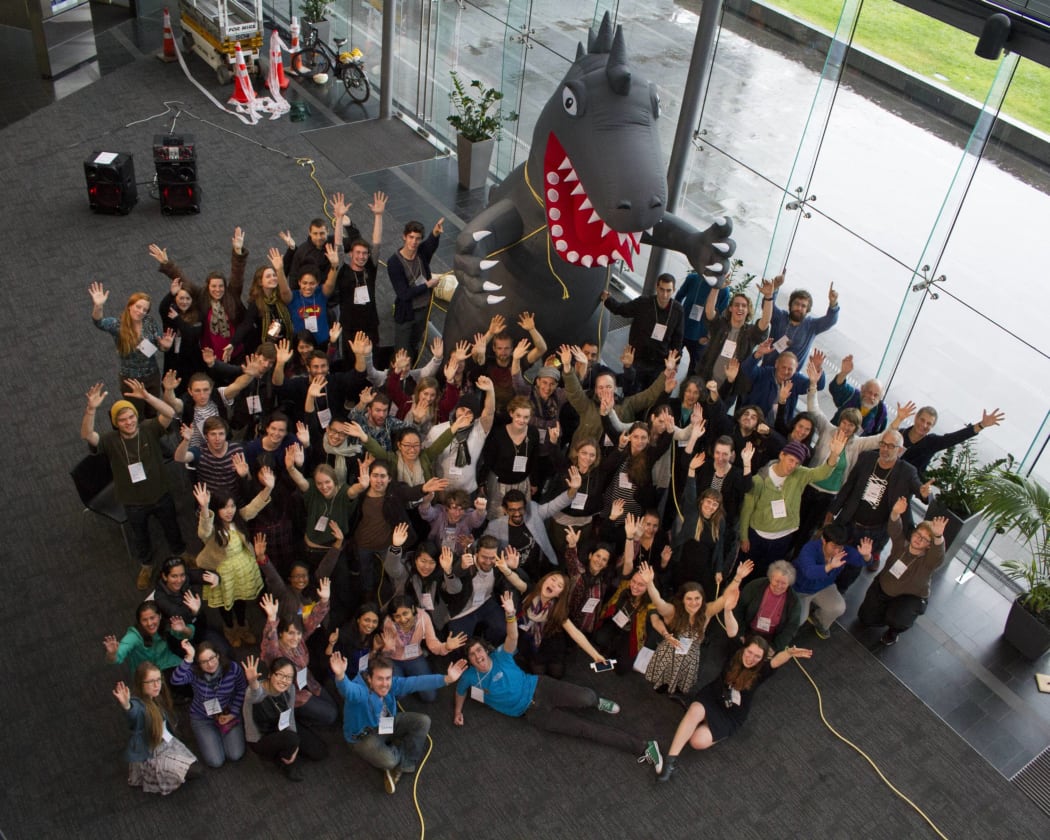 About 100 young people in front of a model of a dinosaur