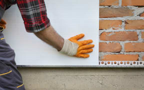 Worker placing styrofoam, polystyrene thermal insulation to brick wall, house renovation