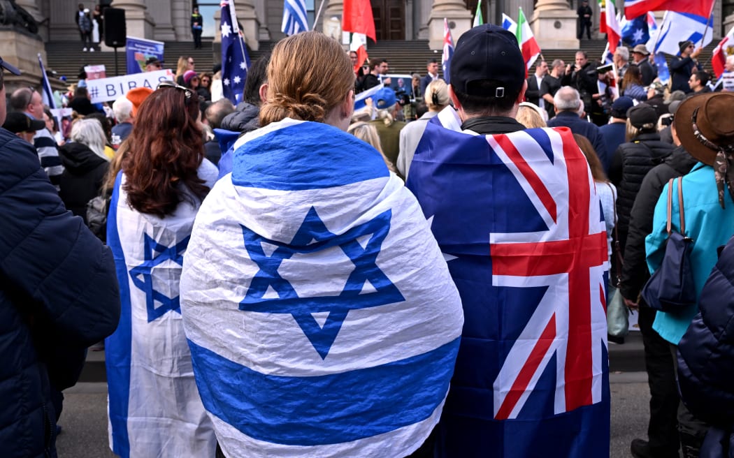 People wearing flags of Israel and Australia listen to speeches at a rally in Melbourne on July 6, 2025, after the front door of a synagogue was set ablaze on July 4. A man suspected of setting fire to an Australian synagogue as worshippers ate dinner inside has been arrested and charged, police said on July 6. (Photo by WILLIAM WEST / AFP)