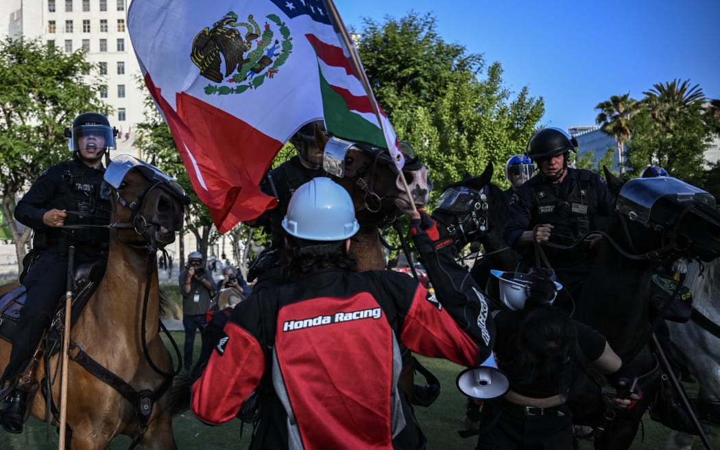 A person waves a combination US and Mexican flag as LAPD officers on horseback clash with protesters gathered near Los Angeles City Hall to protest against federal immigration operations on June 11, 2025. Protests against Donald Trump's harsh immigration policies spread on June 11 across the United States despite a military-backed crackdown in Los Angeles and threats by the hard-right Republican president to use "heavy force." In Los Angeles, where the unrest began on June 6, an overnight curfew intended to keep people out of the downtown area was largely effective, with police arresting around 25 people who had refused to leave. (Photo by RONALDO SCHEMIDT / AFP)