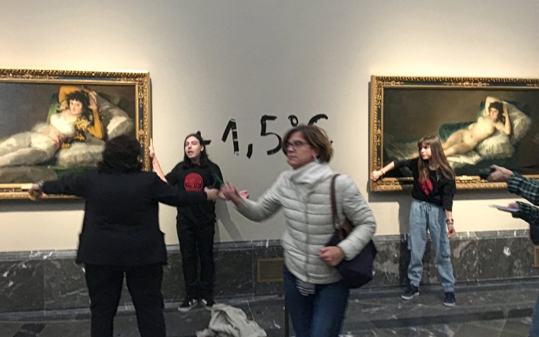 Two activists shown with hands glued to the frames of paintings by Francisco Goya at the Prado museum in Madrid, in a picture released by Extinction Rebellion on 5 November, 2022.