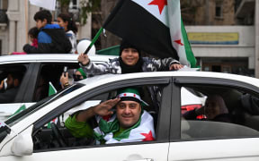 A boy waves a Syrian flag as they celebrate a year since the ousting of longtime ruler Bashar al-Assad in the Syrian capital Damascus on December 8, 2025. President Ahmed al-Sharaa on December 8 urged Syrians to work together to rebuild their country as they marked a year since the ousting of longtime ruler Bashar al-Assad. Sharaa's Islamist-led alliance launched a lightning offensive in late November last year, taking the capital Damascus on December 8 after nearly 14 years of war and putting an end to more than five decades of the Assad family's iron-fisted rule. (Photo by LOUAI BESHARA / AFP)