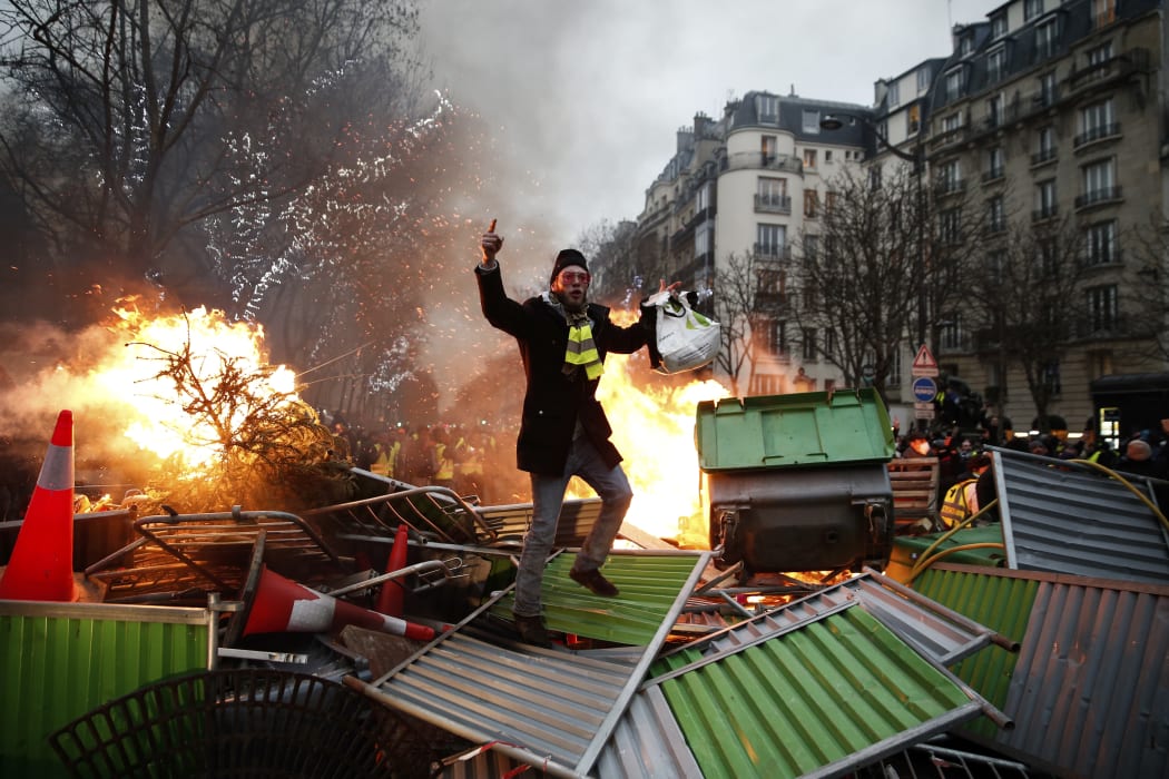 A demonstrator gestures on a burning barricade on January 5, 2019 in Paris, during an anti-government demonstration called by the yellow vest "Gilets Jaunes" movement.