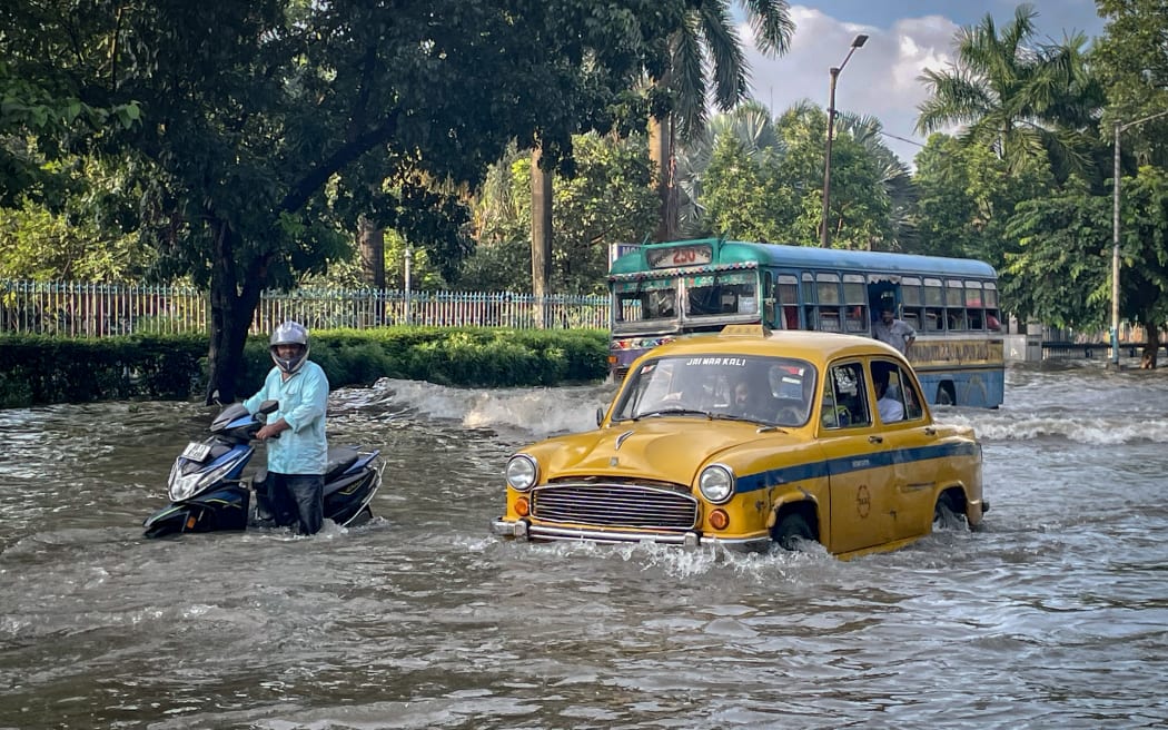 A scooter, bus, and yellow taxi move through a flooded road after heavy rainfall in Kolkata, West Bengal, India, on September 23, 2025. (Photo by Yousuf Sarfaraz/NurPhoto) (Photo by Yousuf Sarfaraz / NurPhoto via AFP)