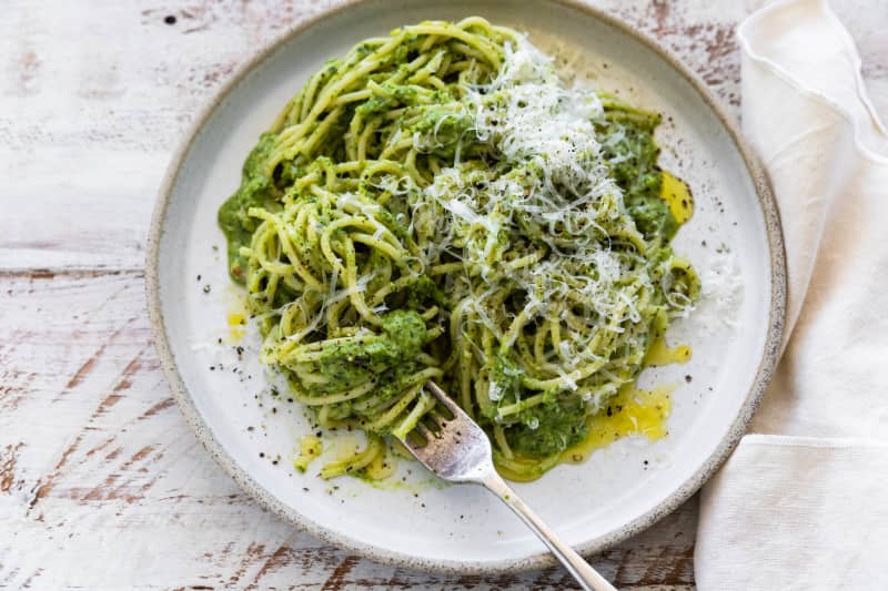 A dish of broccoli spinach pesto pasta garnished with grated parmesan.