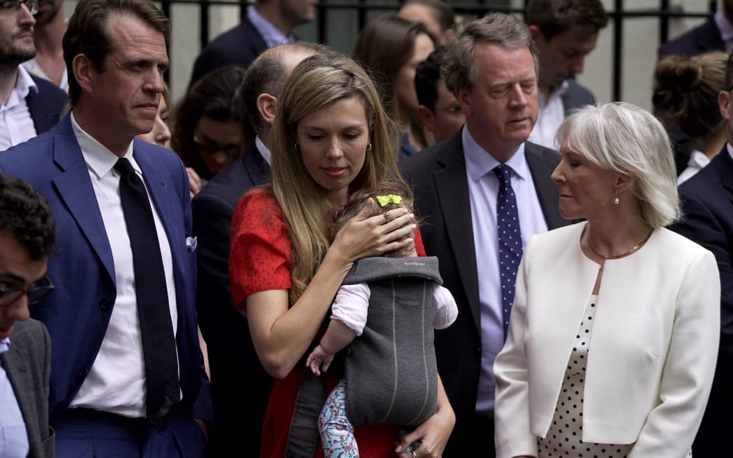 Carrie Johnson, wife of Britain's Prime Minister Boris Johnson, carries their daughter Romy next to Britain's Culture Secretary Nadine Dorries (R), Britain's Conservative party chairman Ben Elliot (L) and Britain's Scotland Secretary Alister Jack (back R) ahead of a statement by the premier in front of 10 Downing Street in central London on July 7, 2022. - Johnson quit as Conservative party leader, after three tumultuous years in charge marked by Brexit, Covid and mounting scandals. (Photo by Niklas HALLE'N / AFP)