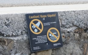 A sign at Ōwhiro Bay warns people not to take shellfish or swim after rain. Karori residents want similar signs to warn people to stay out of the polluted stream, but Wellington Water has refused to erect any.