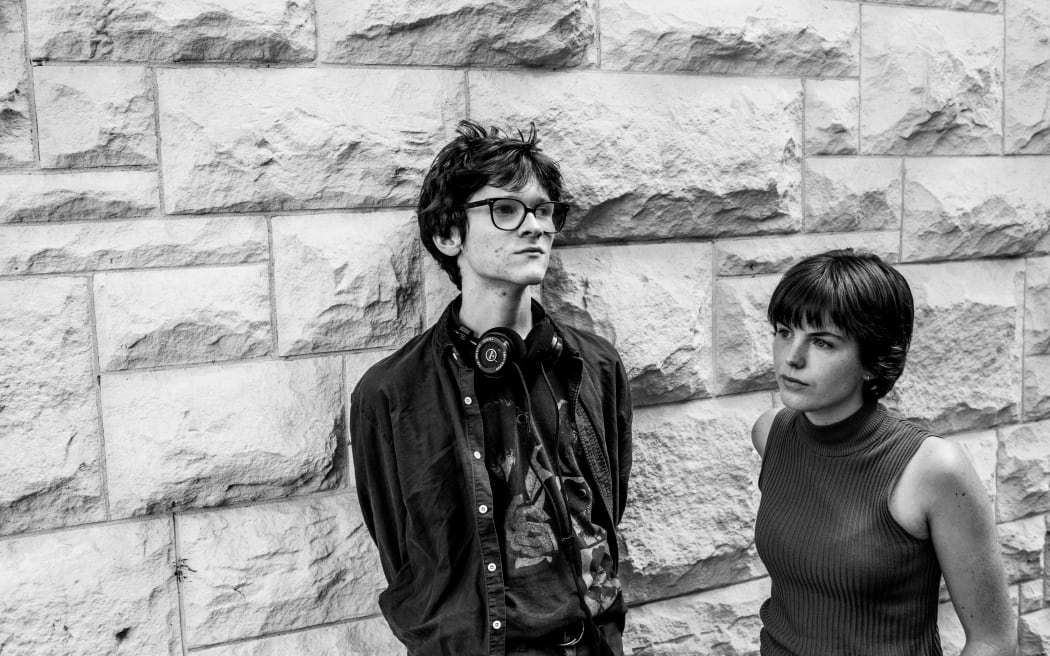 Liam Hansen and Frances Wright, co-hosts of Auckland student radio arts show Various Artists, stand in front of a concrete block wall.
