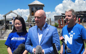Incoming Prime Minister Christopher Luxon (C), with Nancy Lu (L) and MP Andrew Bayly (R) at a media standup in Port Waikato.