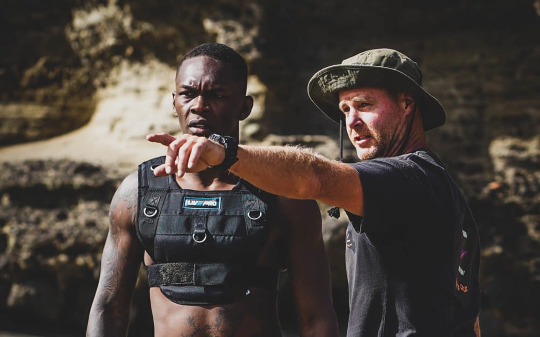 Young man on beach in weighted vest being instructed by coach.