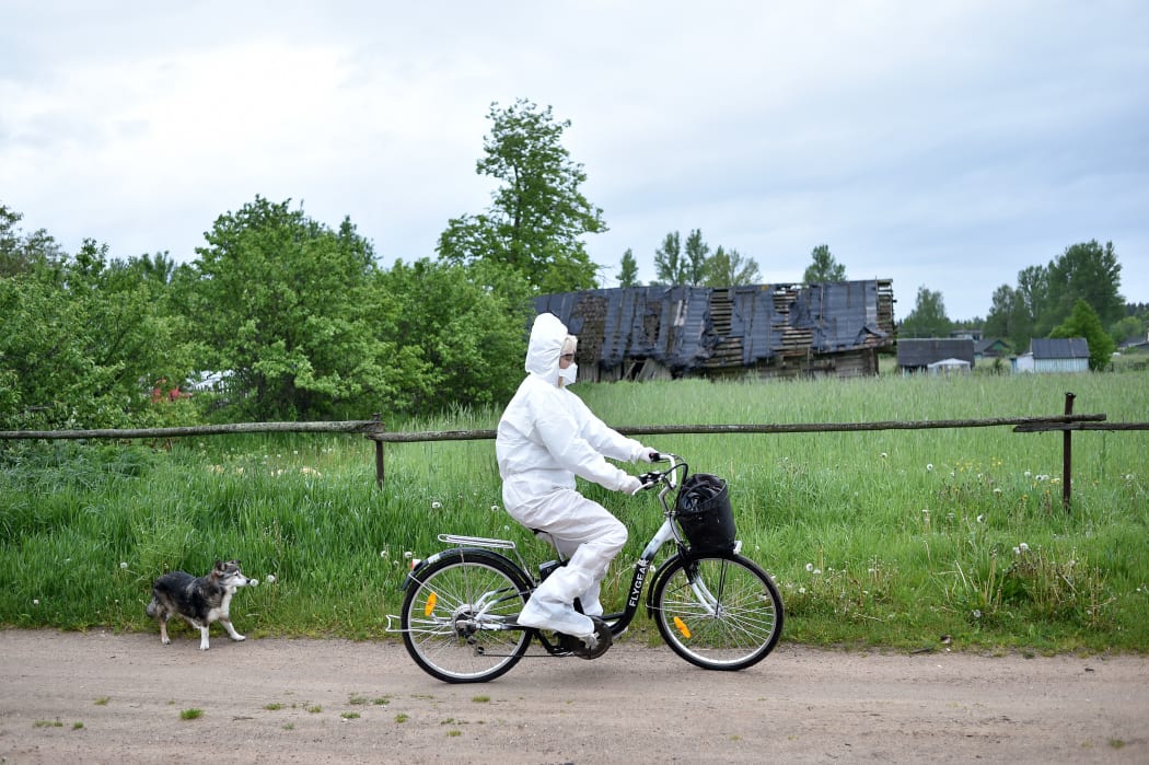 Paramedic Nadezhda Konanava, 65, wearing a protective suit rides her electric bike at the village of Novaya Obo.