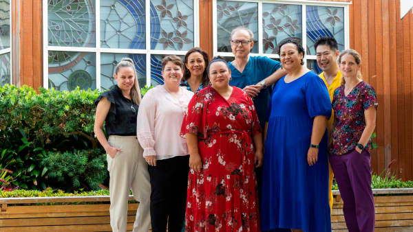 A group of eight smiling people in colourful clothes.