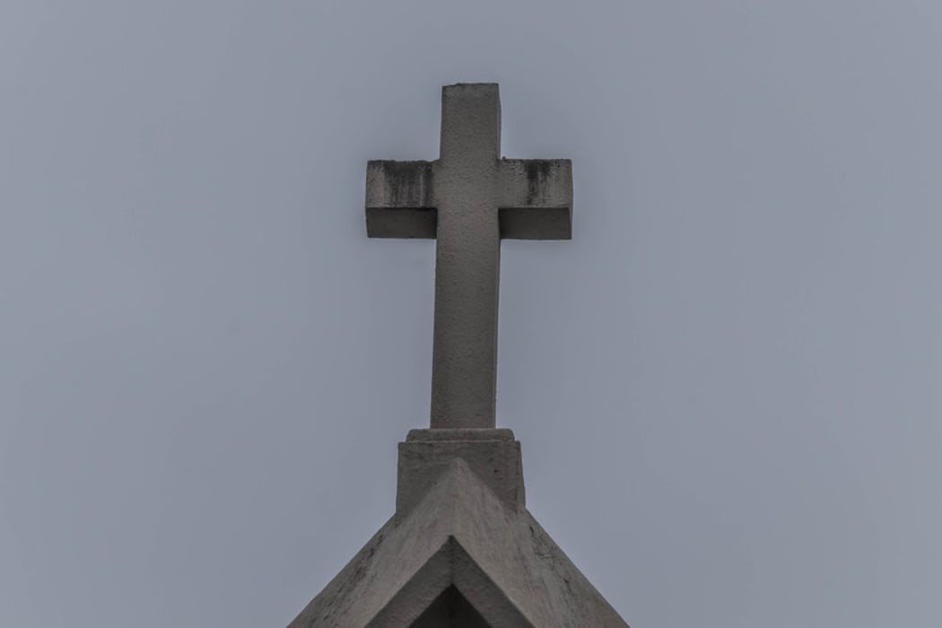 Catholic church steeple with cross on top, sky as background.