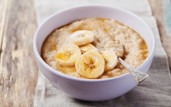 Bowl of oatmeal porridge with banana and caramel sauce on rustic table, hot and healthy breakfast every day, diet food