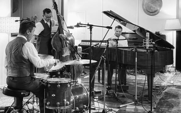 An album cover for the album Exit 430. In a black and white image, Mark Lockett plays drums on the left, Daniel Yeabsley plays double bass in the middle, and Ayrton Foot plays a grand piano on the right.
