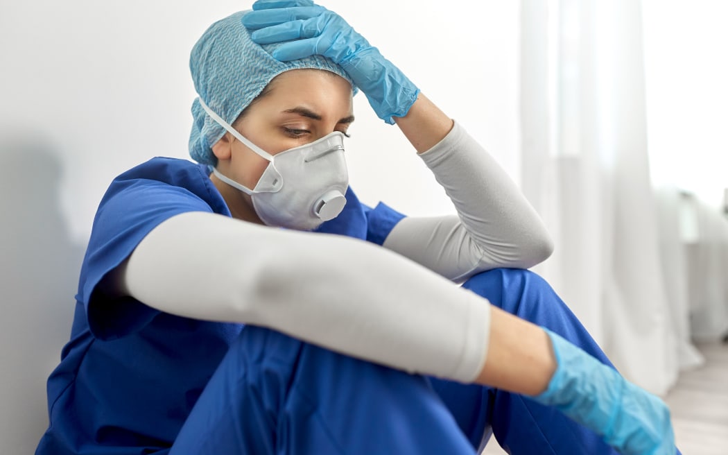 medicine, healthcare and pandemic concept - sad young female doctor or nurse wearing face protective mask or respirator for protection from virus disease holding to head