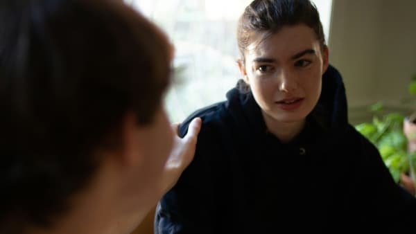 A person consoles and puts their hand on a woman's shoulder as they chat at a table.