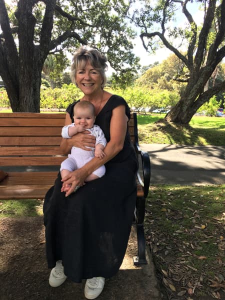 Julie Biuso with her first granddaughter, Remi, in her lap, sitting at a bench in the Parnell Rose Gardens, Auckland.
