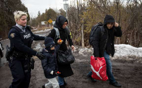 A family of three is escorted to a police vehicle by a Royal Canadian Mounted Police officer after they illegally crossed into Hemmingford, Quebec from the US.
