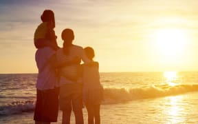 Family standing on a beach looking at the sunset. (file).
