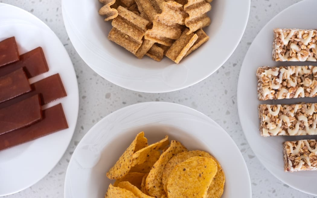 Snack foods on a kitchen bench. Fruit sticks, chips and museli bars.