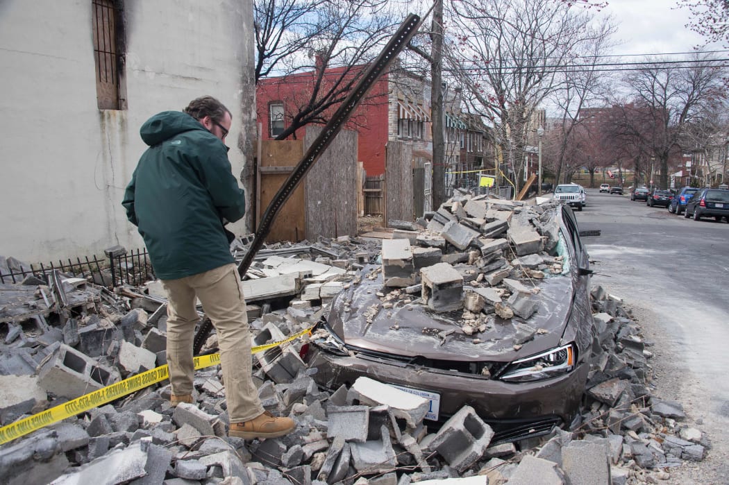 An insurance company employee checks the damage to a car after a partially burnt building collapsed due to strong winds in Northeast Washington, DC, on March 2, 2018.
