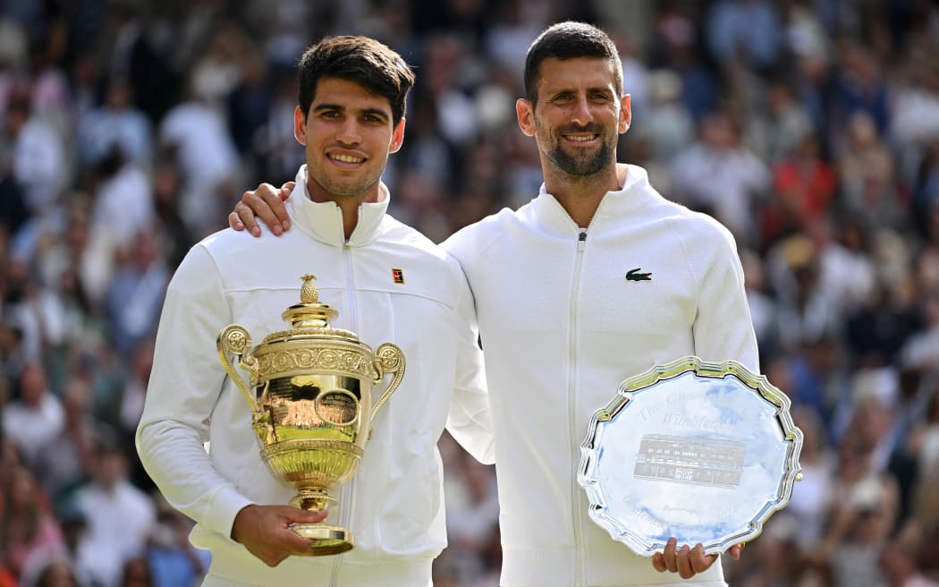 Spain's Carlos Alcaraz holding the winner's trophy (L) and second-placed Serbia's Novak Djokovic pose for pictures during the price ceremony at the end of their men's singles final tennis match on the fourteenth day of the 2024 Wimbledon Championships at The All England Lawn Tennis and Croquet Club in Wimbledon, southwest London, on July 14, 2024. Defending champion Alcaraz beat seven-time winner Novak Djokovic in a blockbuster final, with Alcaraz winning 6-2, 6-2, 7-6. (Photo by ANDREJ ISAKOVIC / AFP) / RESTRICTED TO EDITORIAL USE