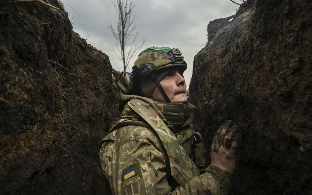 A Ukrainian serviceman takes cover in a trench during shelling next to a 105mm howitzer  near the city of Bakhmut, on March 8, 2023, amid the Russian invasion of Ukraine. (Photo by Aris Messinis / AFP)