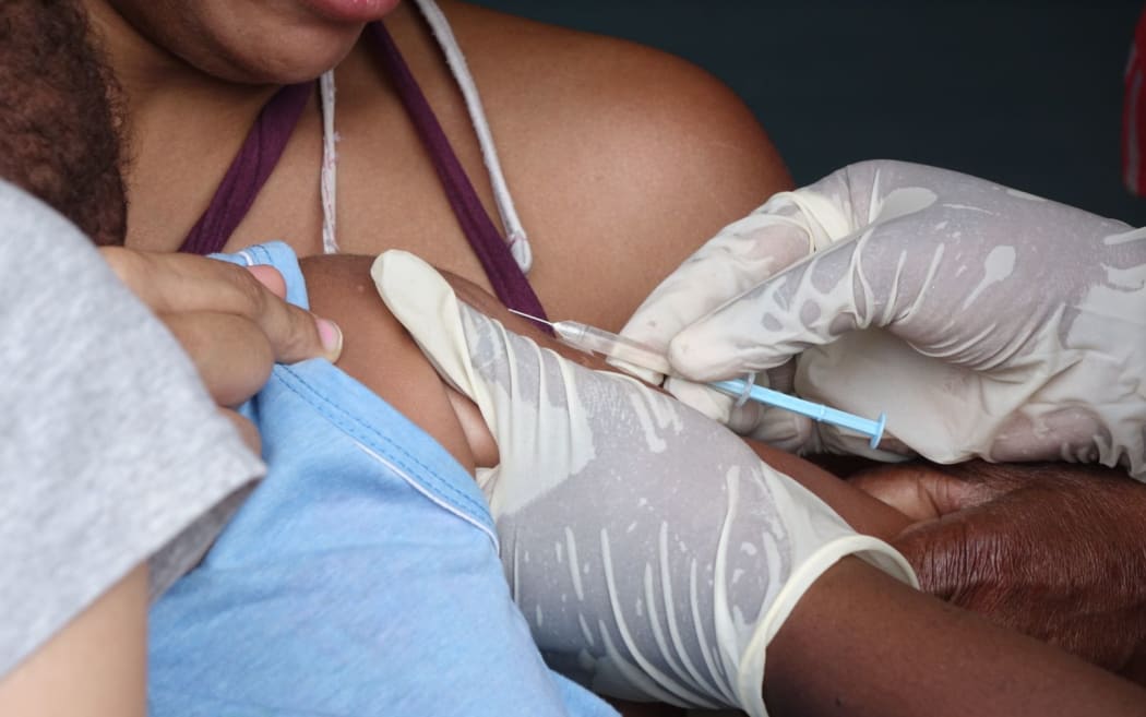 A child is vaccinated by an aid worker.