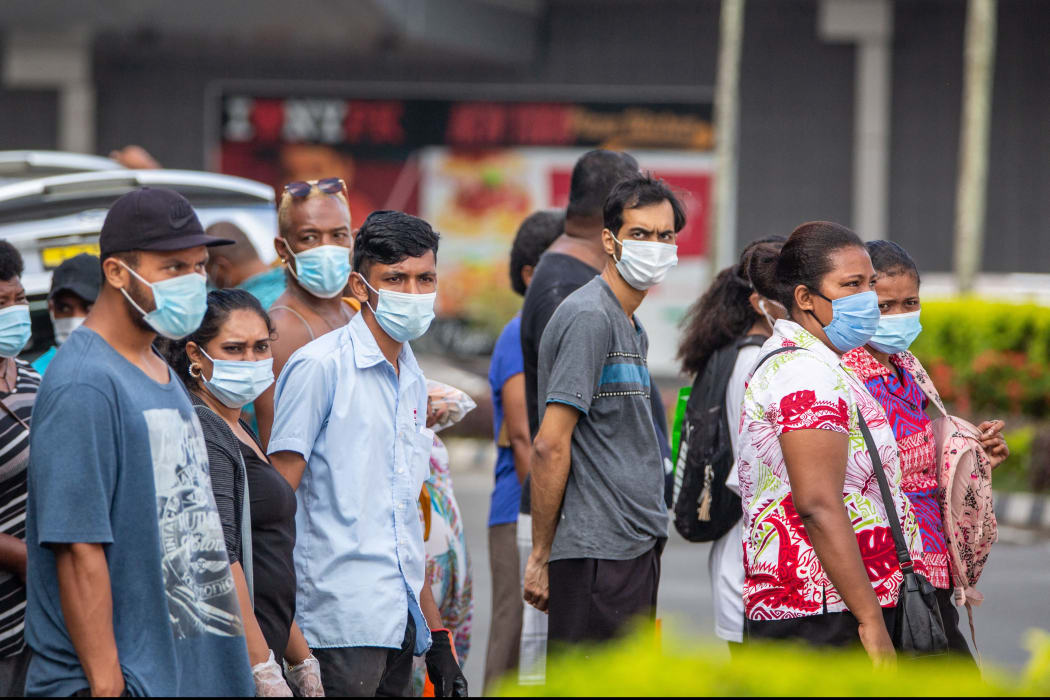 This picture taken on April 24, 2021 shows residents wearing face masks waiting to cross the main road in the Fijian capital Suva ahead of an expected lockdown in the capital due to a Covid-19 spike. (Photo by Leon LORD / AFP)