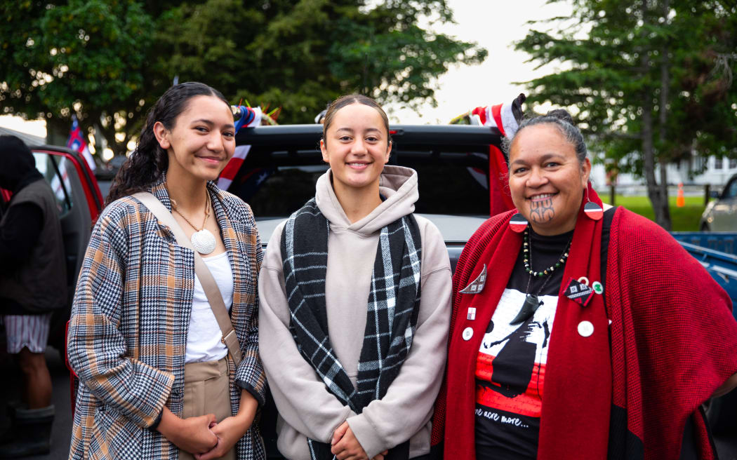 Three wāhine stand in the carpark of Te Kamaka Marae on Auckland's North Shore. From left to right, Rangimarie Te Whenua, Chelsea Reti, and Jo Murray, all smiling.