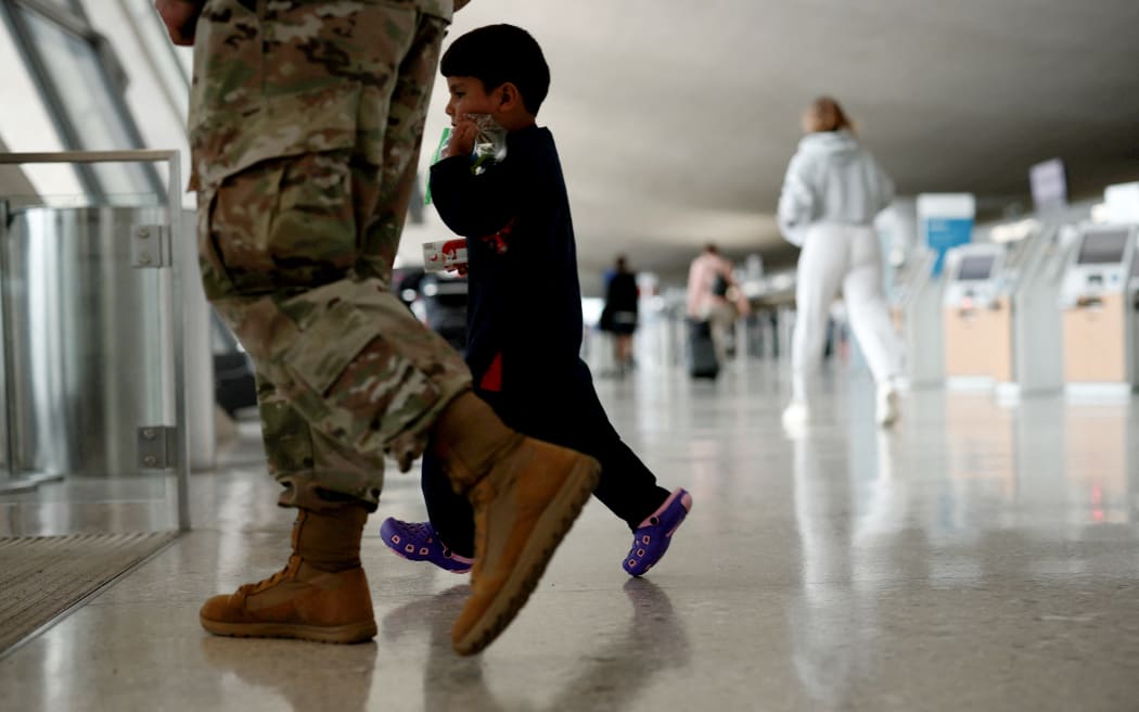 DULLES, VIRGINIA - AUGUST 31: An Afghan boy walks with a U.S. service member as he and his family are led through the Dulles International Airport to board a bus that will take them to a refugee processing center after being evacuated from Kabul following the Taliban takeover of Afghanistan on August 31, 2021 in Dulles, Virginia. The Department of Defense announced yesterday that the U.S. military had completed its withdrawal from Afghanistan, ending 20 years of war.   Anna Moneymaker/Getty Images/AFP (Photo by Anna Moneymaker / GETTY IMAGES NORTH AMERICA / Getty Images via AFP)