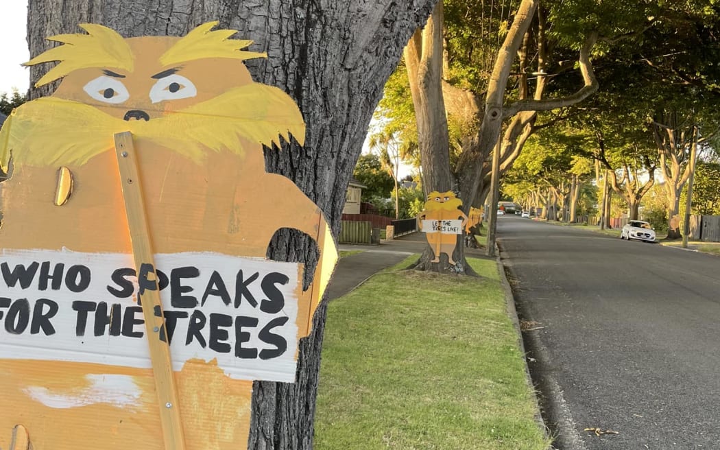 A picture of the Dr Seuss character Lorax holding a sign that says "Who speaks for the trees". The sign is in front of trees that are due to be cut down in Christchurch