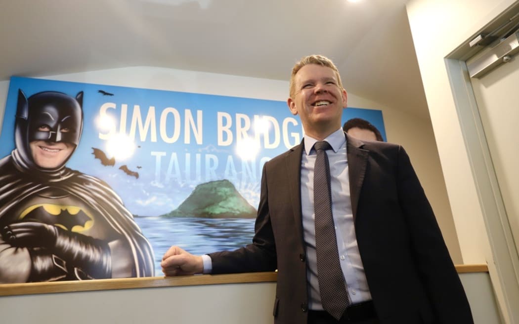 Chris Hipkins in front of poster of John Key as Batman at McIndoe dental clinic in Tauranga.