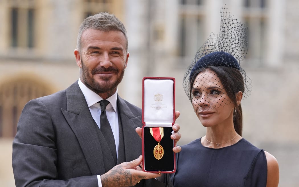 Former England footballer David Beckham (L) poses next to his wife, singer and fashion designer Victoria Beckham (R), with his medal after being appointed as a Knight Bachelor (Knighthood) for services to sport and charity at an investiture ceremony at Windsor Castle on 4 November, 2025.