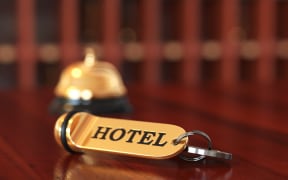 Close up of room access key and bell on wooden reception desk. Soft focus illustration