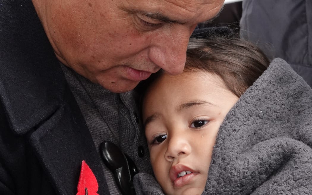 Purcell Turner protects his moko Jershon from a bitterly cold wind as he waits to collect his grandfather’s medals.
