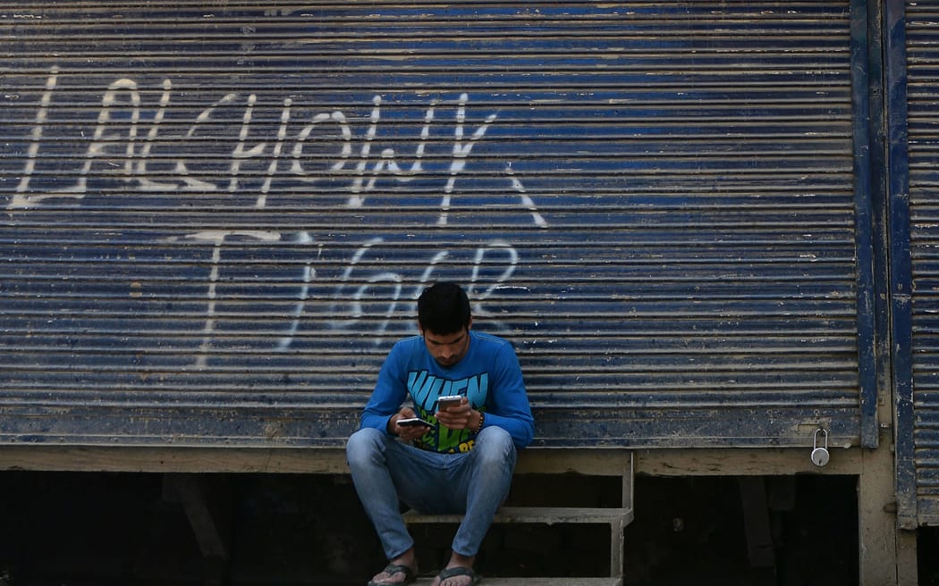 A Kashmiri man looks at his mobile phones in front of shuttered shops in Srinagar.