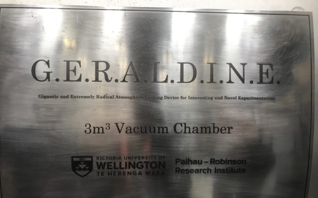 A close up of a metallic surface with the words 'G.E.R.A.L.D.I.N.E. Gigantic and Extremely Radical Atmosphere-Lacking Device for Interesting and Novel Experimentation. 3m3 vaccum chamber. Victoria University of Wellington Te Herenga Waka Paihau Robinson Reserach Institute.'
