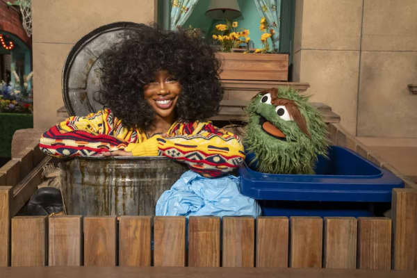 A smiling woman with an afro poses with a green puppet.