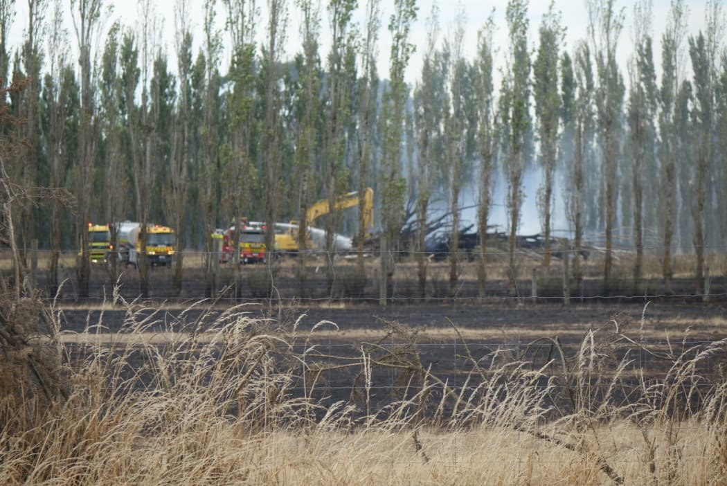A digger and fire engines attack the rubbish pile from the ground.