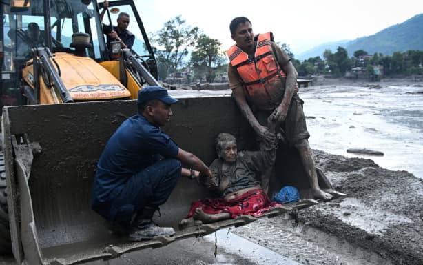 Rescuers use an excavator to transport a flood survivor, following flash floods and a landslide disaster in Devghat, in the Nepal's Nuwakot district on August 26, 2026. A massive flood and landslide disaster on the Nepal-Tibet border killed at least 103 people on August 26, 2026 and left several hundred missing, many of them foreign tourists. Aid workers said entire settlements had been "wiped out". Some 403 tourists -- 341 of them foreigners -- were unaccounted for several hours after the disaster struck, according to the tourism ministry. (Photo by PRAKASH MATHEMA / AFP)