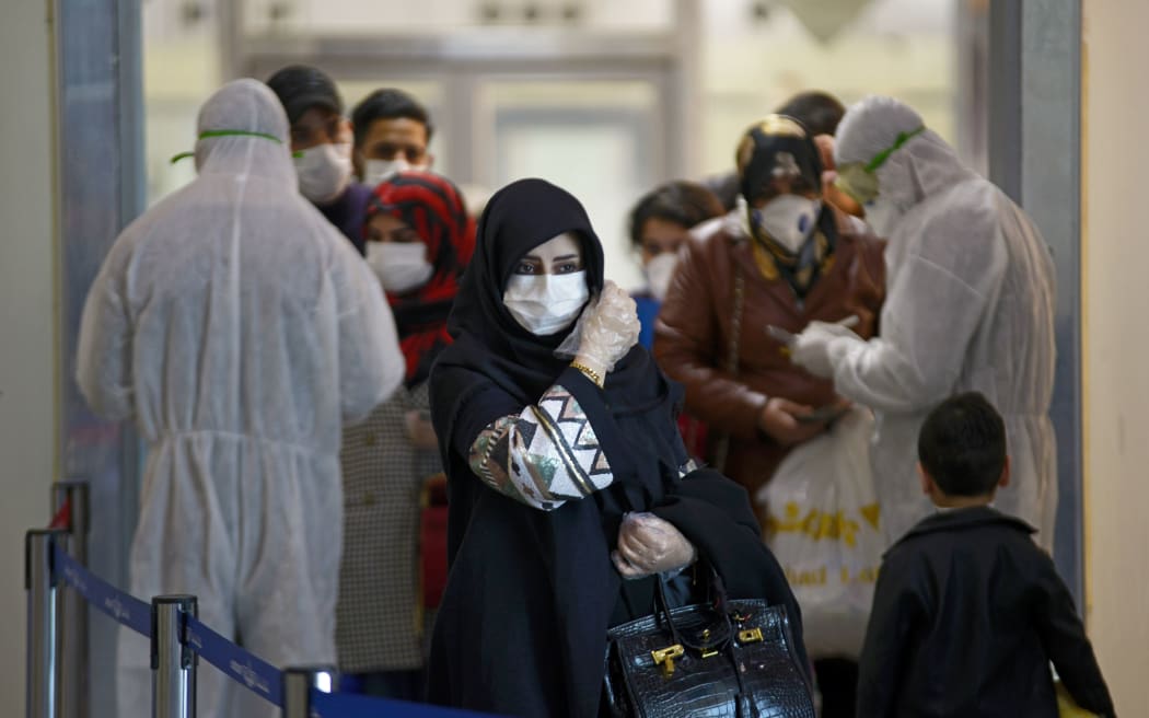 Medical staff in protective gears distribute information sheets to Iraqi passengers returning from Iran at Najaf International Airport on March 5, 2020.