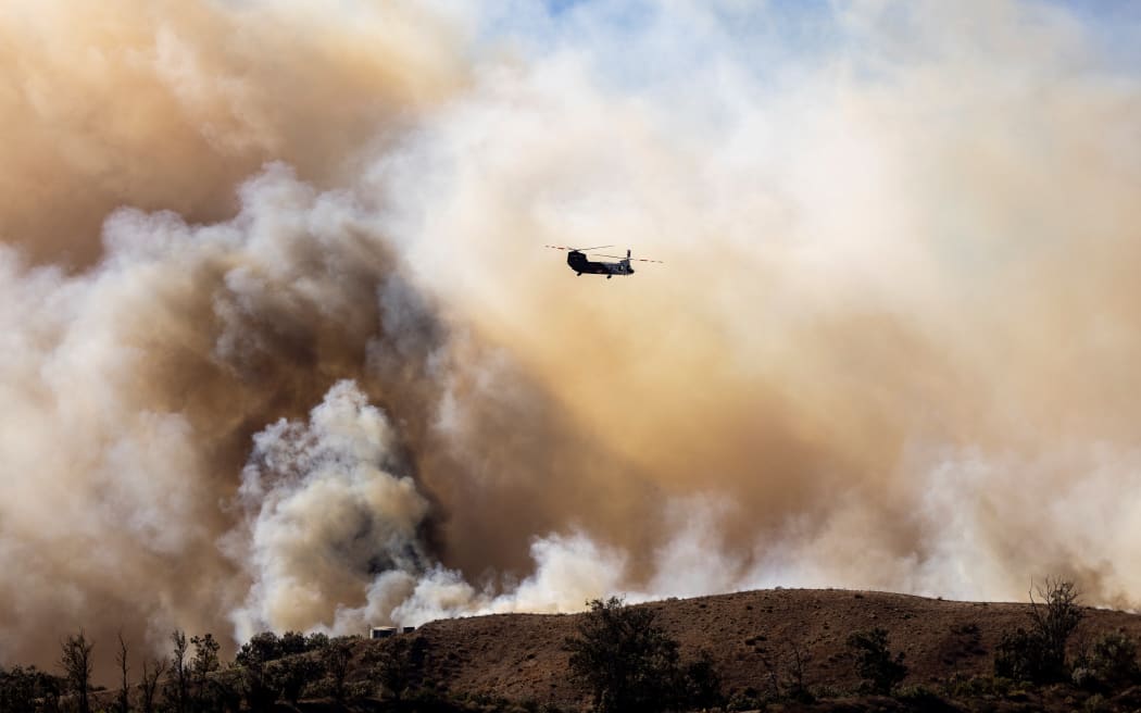 A fire helicopter flies toward the Mountain Fire’s plume as it scorches acres, the wildfire fueled by strong Santa Ana winds, in Moorpark, California, on November 7, 2024. - Thousands of people were urged to flee an out-of-control wildfire burning around communities near Los Angeles on November 7, with scores of homes already lost to the fast-moving flames.
Fierce seasonal winds had cast embers up to three miles (five kilometers) from the seat of the fire around Camarillo, with new spots burning on hillsides, farmland and in residential areas.
The Mountain Fire grew rapidly from a standing start early November 6, and by the following day had consumed 20,485 acres (8,290 hectares), with towering flames leaping unpredictably and sending residents scrambling. (Photo by ETIENNE LAURENT / AFP) / “The erroneous mention[s] appearing in the metadata of this photo by ETIENNE LAURENT has been modified in AFP systems in the following manner: [Moorpark] instead of [Santa Paula]. Please immediately remove the...